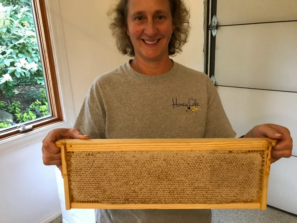 Person holding wooden honeycomb frame indoors.